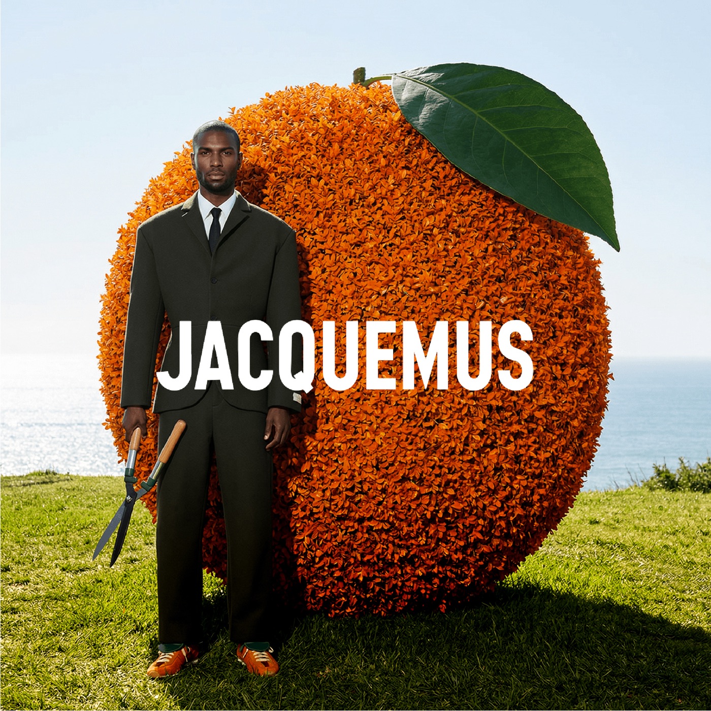 Jacquemus — suited silhouette before a giant orange in a landscape